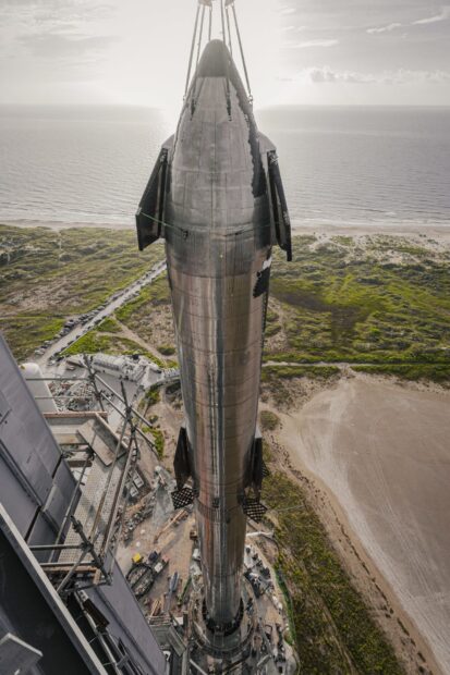 A large starship standing on the launchpad overlooking the coastline and surrounding landscape