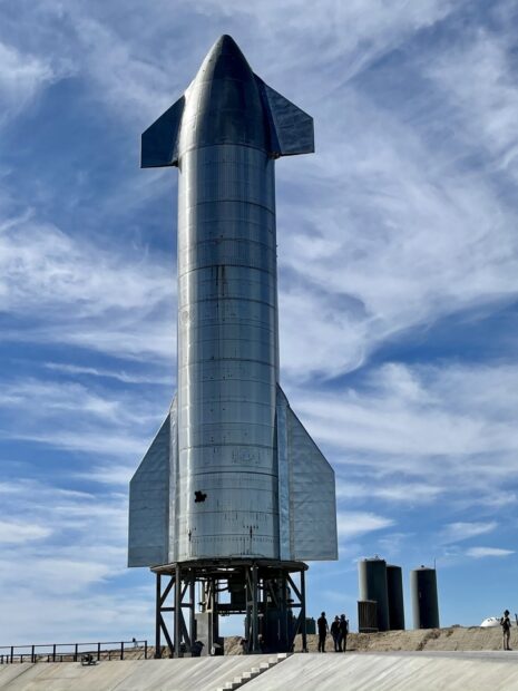 A shiny starship standing on a launch pad under a partly cloudy sky
