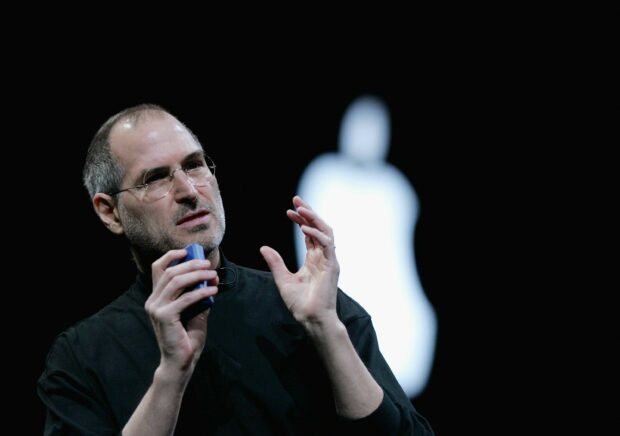 Steve Jobs giving a presentation with a blurred Apple logo in the background