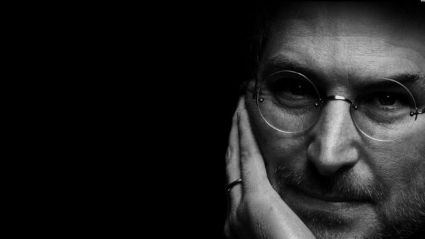 Close up of Steve Jobs wearing round glasses and resting his face on hand in black and white portrait