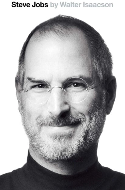 Steve Jobs with round glasses and beard smiling in a black turtleneck shirt