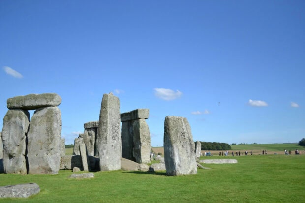 Ancient stone formations of Stonehenge standing on green grass under a clear blue sky