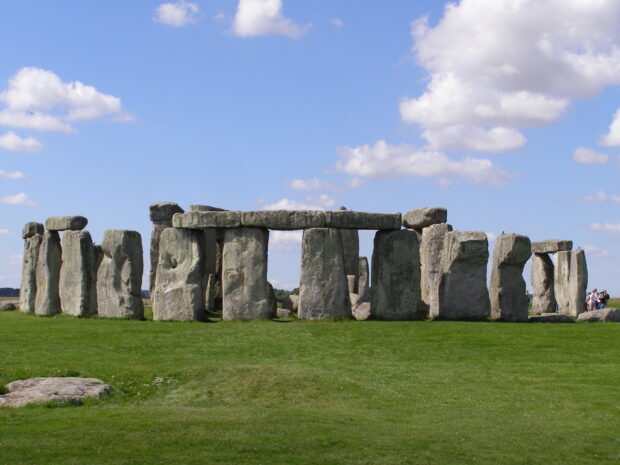 Ancient Stonehenge structure on a green field under a bright blue sky