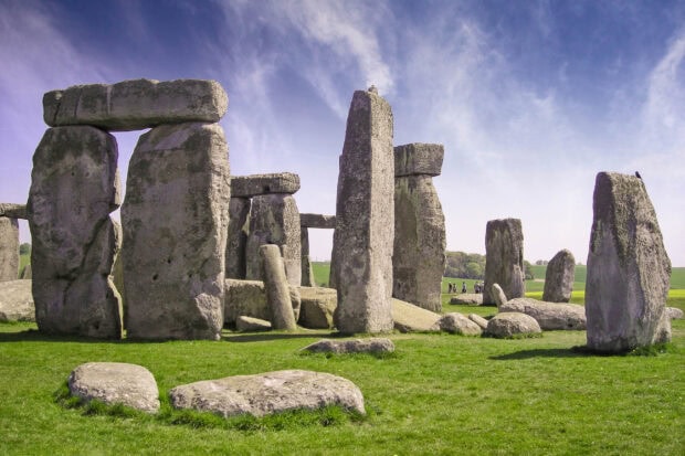 Ancient stone monuments at Stonehenge standing on green grass under a blue sky