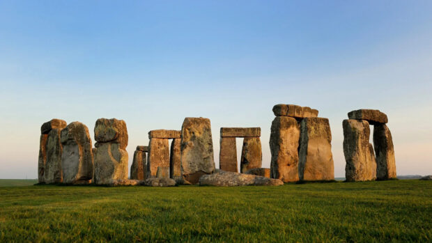 Ancient Stonehenge monument standing on green grass under a clear blue sky