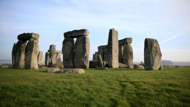 Ancient Stonehenge monument standing on green grass under a clear sky