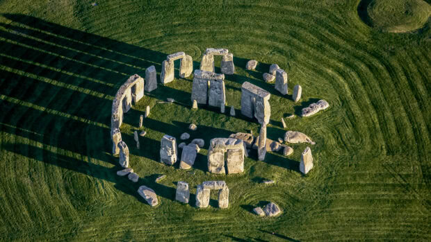 Aerial view of Stonehenge ancient stone monument casting long shadows on green grass field