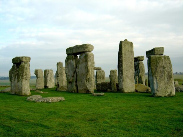 Ancient Stonehenge monument stones standing on green grass under cloudy sky