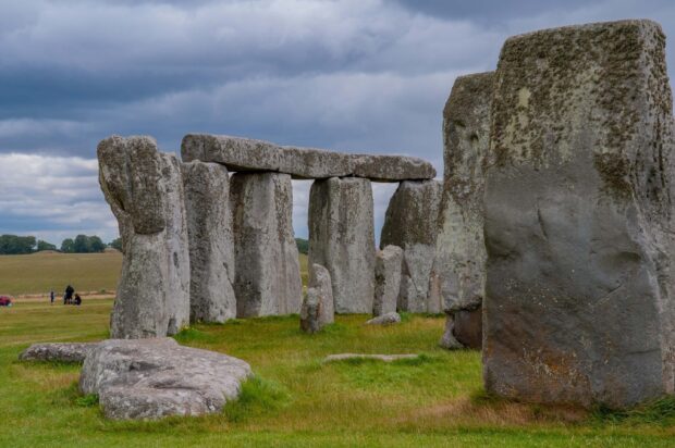 Ancient Stonehenge formation standing on green grass under a cloudy sky