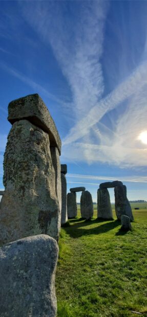 Ancient Stonehenge structure under blue sky with clouds and sun