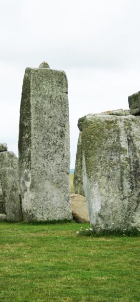 Ancient Stonehenge monoliths standing on green grass under cloudy sky