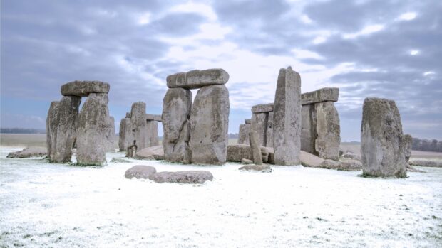 Ancient Stonehenge stones covered with snow under cloudy sky in winter