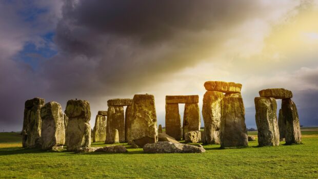 Stonehenge monument under dramatic sky at sunset with sunlight illuminating the stones
