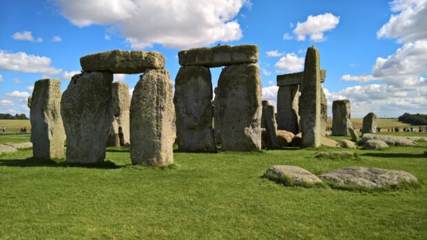 Ancient Stonehenge monument stands tall on green grass under blue sky