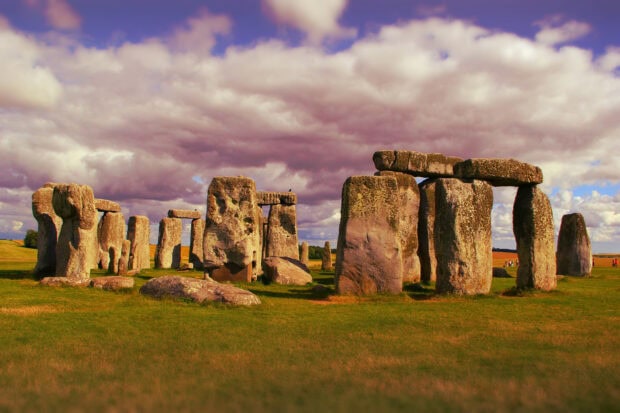 Ancient Stonehenge arrangement standing tall on grassy field under cloudy sky