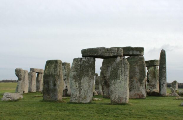 Ancient Stonehenge monument stands on green field under a cloudy sky