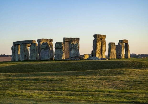 Ancient Stonehenge monument surrounded by green grass under clear sky