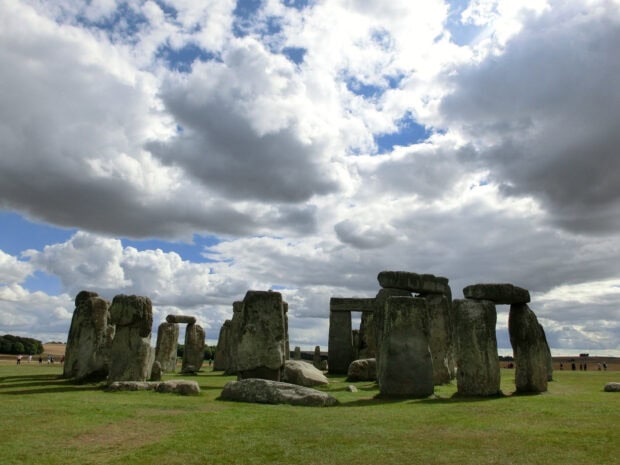 Ancient Stonehenge monument under a cloudy sky on a green field