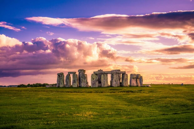 Ancient Stonehenge standing under a colorful sky during sunset on a green field
