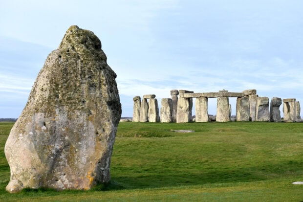A large stone with Stonehenge standing on a grassy field in the background