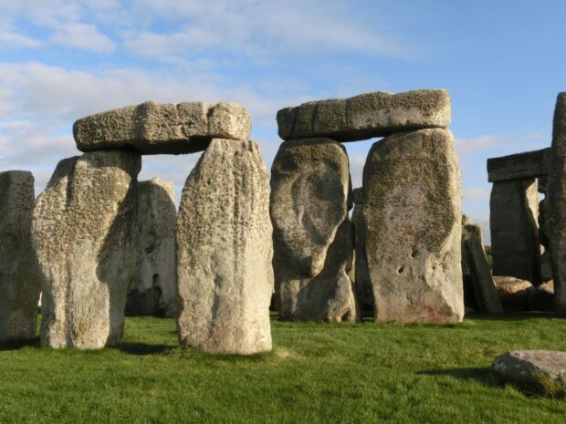 Ancient Stonehenge stones standing on green grass under a partly cloudy sky