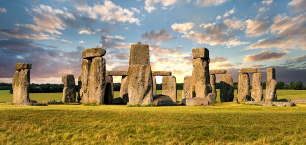 Ancient Stonehenge structure under a cloudy sky in a grassy field at sunset