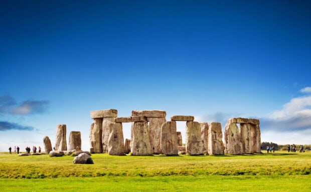 Stonehenge ancient monument under a clear blue sky with green grass around
