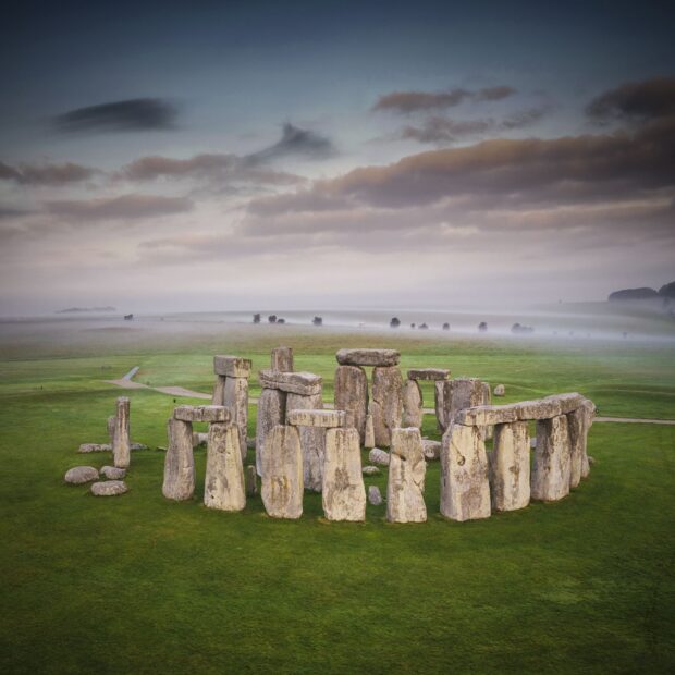 Ancient Stonehenge monument surrounded by misty green fields at dawn