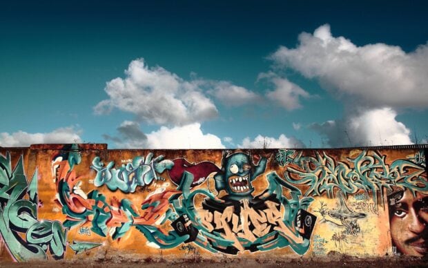 Colorful street art with cartoon character and abstract graffiti on an urban wall under cloudy sky