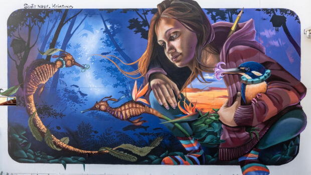 A girl in a hoodie closely observing marine life in a creative street art mural