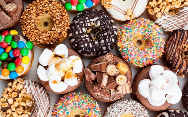 Assorted sweets covered donuts with colorful toppings and chocolate pieces on a flat surface