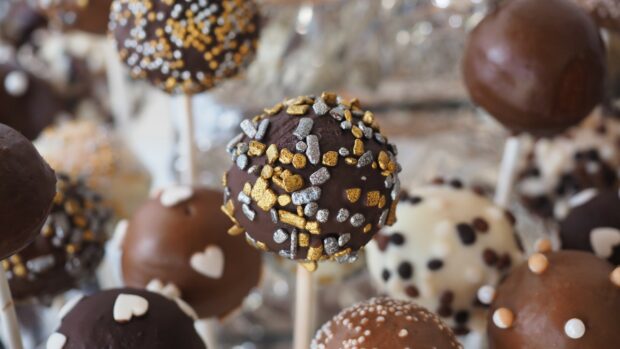 Chocolate cake pops with colorful sprinkles on sticks in focus