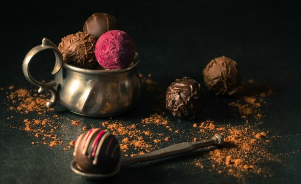 A close up of assorted sweets in a metal cup and on a spoon surrounded by cocoa powder