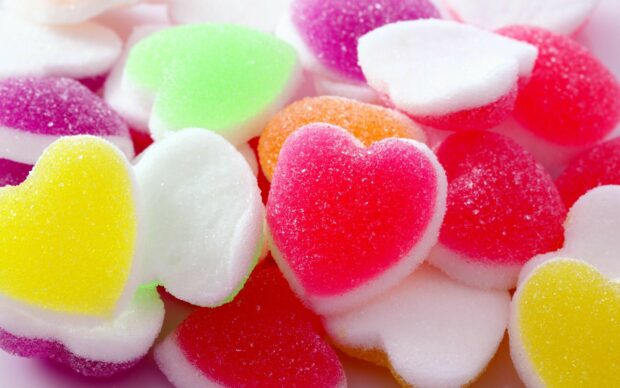 Colorful heart shaped sweets covered with sugar crystals on a bright surface