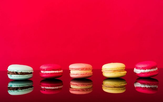 Colorful macarons arranged in a row with a red background and their reflection on a shiny surface