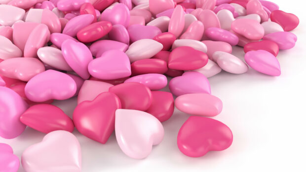 Pink and red heart shaped sweets scattered on a white surface creating a colorful arrangement