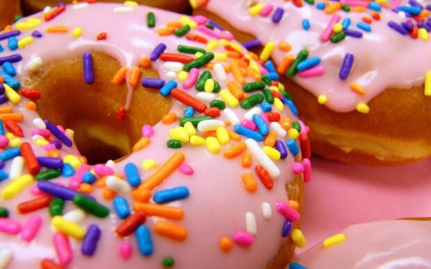 Close up of colorful sprinkles on pink frosted donuts with sweets