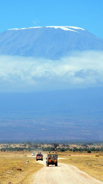 Safari vehicles traveling on Tanzania savannah with Kilimanjaro mountain in the background