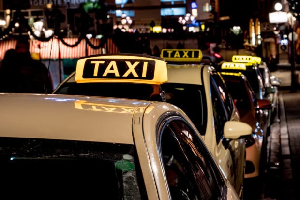 A row of taxis waiting in the city at night with illuminated taxi signs