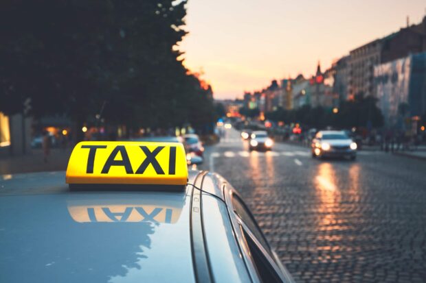 A taxi sign on a car roof with a city street and cars in the background at sunset