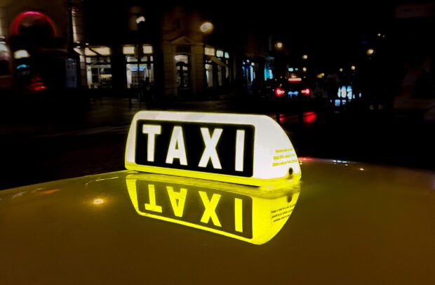 Illuminated taxi sign reflected on the roof of a yellow taxi at night in the city
