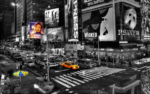 Yellow taxi driving through a busy city street with illuminated billboards at night