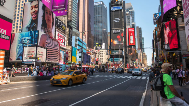 Yellow taxi driving on a busy city street with tall buildings and advertisements