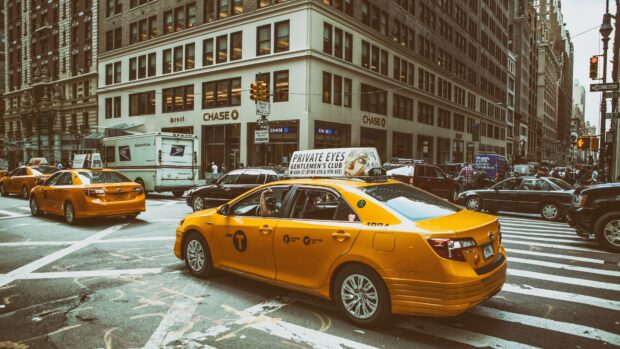 Yellow taxi driving through busy city street with urban buildings and traffic signs