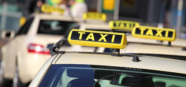 A row of yellow taxi signs on several cream colored cars waiting in line