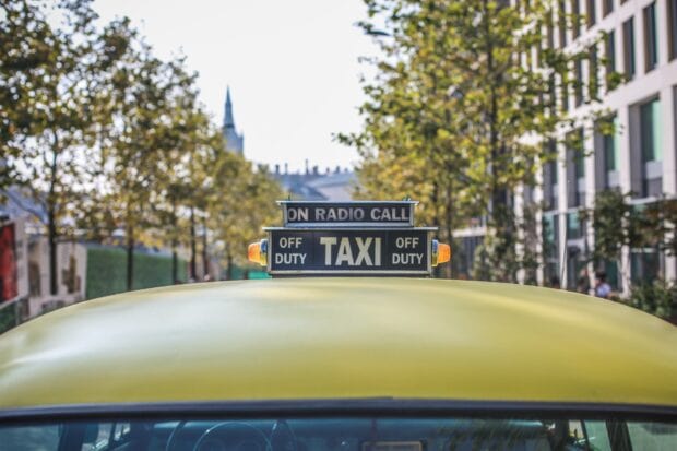 A yellow taxi off duty sign on the top of a taxi car in a city street
