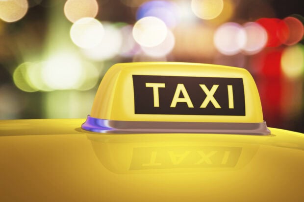 Close up of a taxi sign on top of a yellow taxi car with blurred city lights in the background
