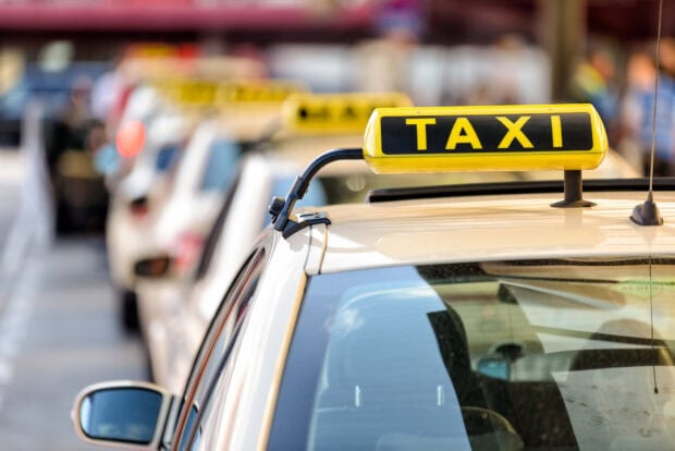 A row of taxis with clear taxi signs waiting in line on the street