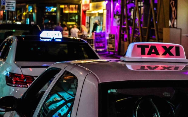 White taxi cars with illuminated taxi signs parked on a city street at night