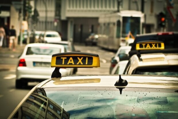 Yellow taxi sign on a busy city street with multiple cars in traffic